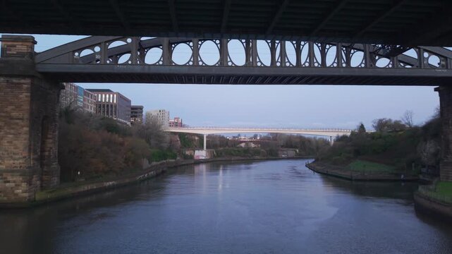 Aerial drone shot flying backward over the River Wear at dawn, retreating from the Wearmouth Bridge and Monkwearmouth Railway Bridge to reveal the modern Keel Crossing