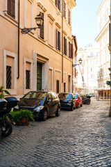 Obraz premium Cars and scooters parked on a cobblestone street in a historic city during the day