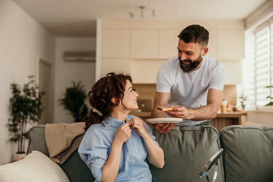 Husband bringing breakfast in bed to smiling wife