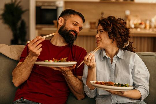 Happy couple enjoying takeout food on sofa at home