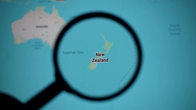 Map of New Zealand under magnifying glass highlighting islands and Tasman Sea context. Tourism, Maori culture, English language links with Australia economy relationship and sports identity.