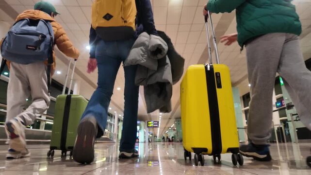 Mother and two children walking with suitcases in an airport terminal, low-angle rear view of the family heading towards the boarding gate for their vacation flight