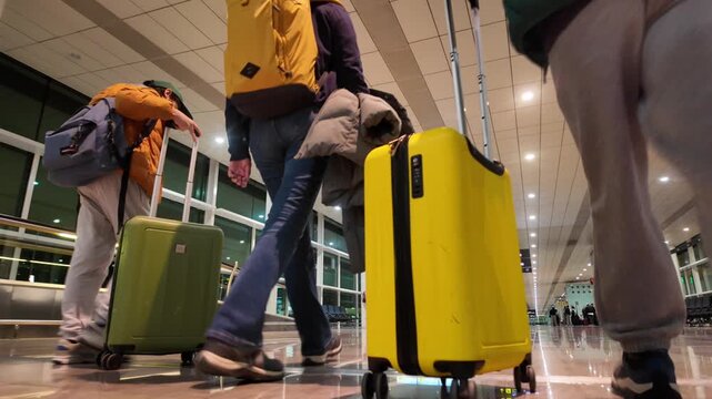 Low-angle view of a traveling family with suitcases walking through an airport terminal, heading towards the boarding gate for their vacation journey and departure