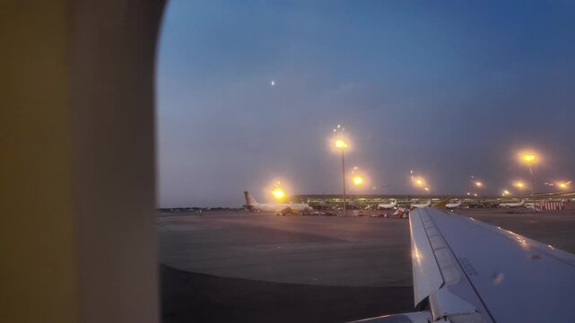 Airplane taxiing on the runway before takeoff, passenger's point of view from the window with the wing visible during a beautiful night with the moon in the blue sky