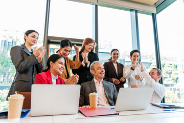 Fototapeta premium Diverse office team celebrates a successful meeting, smiling and applauding around laptops in a bright conference room with city views.