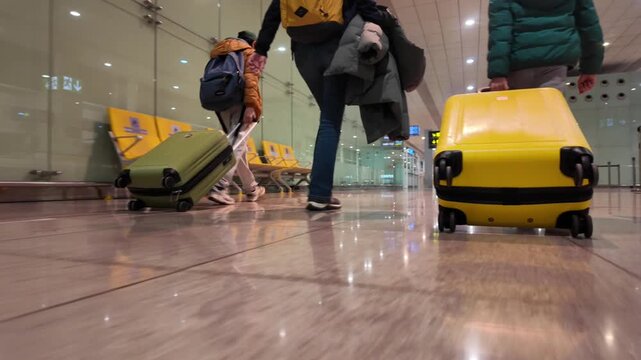 Low angle view of a family with luggage walking through an airport terminal, the yellow suitcase following the group of travelers as they depart for their vacation trip