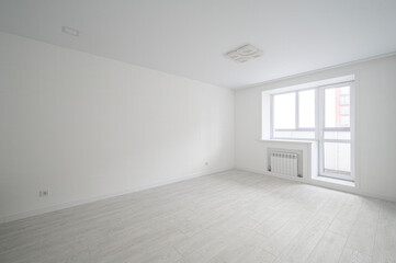 Fototapeta premium bright, minimalist room with white walls and ceiling, light wooden flooring, a large window with a radiator, and a modern ceiling light fixture. Clean, airy space, ready for furnishing