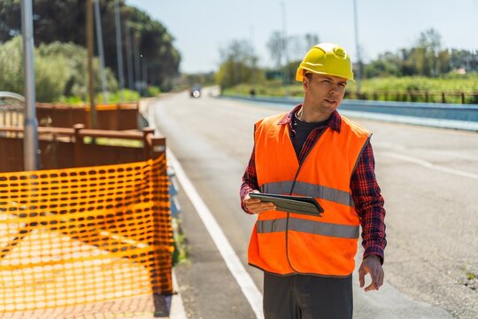 Road construction worker using tablet near safety barrier on asphalt road