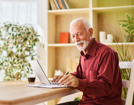 Portrait of a senior mature man or businessman having a video call on laptop in his home office at home