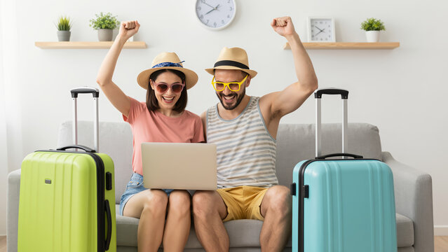 Couple Celebrating Successful Online Travel Booking on a Modern Sofa for Travel Blogs, Vacation Planning, and Lifestyle Marketing