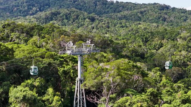 Aerial view of skyrail rainforest cableway in Kuranda Cairns moving over lush tropical green forest canopy under sunlight.