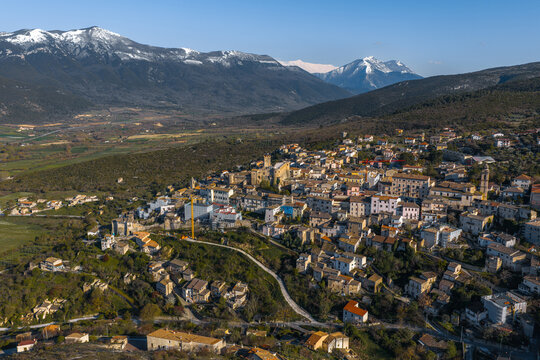 Aerial view of the historic town of Capestrano with the Piccolomini Castle and snow-capped Apennine mountains in the background, Capestrano, Abruzzo, Italy.