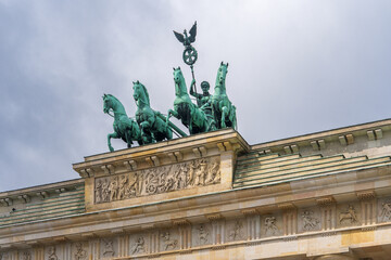 Fototapeta premium Brandenburg Gate in Berlin with a bronze classical two‑wheeled chariot atop, driven by the goddess Victoria, symbolizing peace and triumph, one of Germany’s iconic symbols.Berlin,Germany.