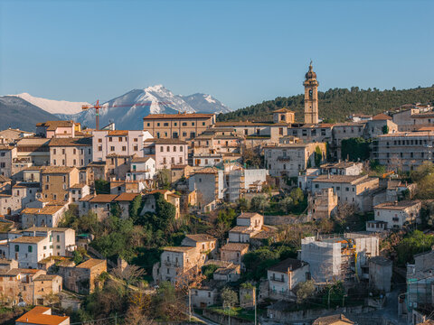 Aerial view of the historic stone buildings and church bell tower of Capestrano with snow-capped mountains in the background Capestrano, Abruzzo, Italy.