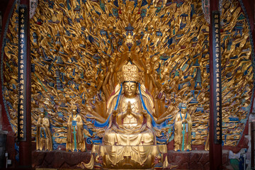 Obraz premium Golden Buddha seated under radiant, elaborate crown. Vibrant, detailed background features intricate, branching golden motifs. Blue and gold drapery frames serene, meditative Buddha figure
