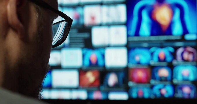 Side view of a man wearing glasses looking at multiple medical imaging screens, representing diagnostics, data analysis, and modern healthcare technology.