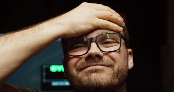 Close-up of a smiling man with glasses touching his forehead, expressing relief, mild stress release, or a moment of realization in a casual setting.