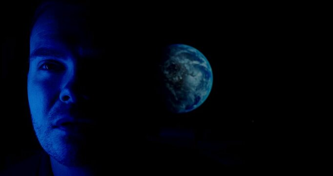 Dark cinematic scene showing half of a human face illuminated in blue light with planet Earth floating in the background, symbolizing connection between humanity, technology, and the universe.