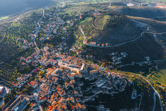 Aerial view of the historic hilltop town with its stone architecture and terracotta roofs nestled among the rolling hills and olive groves of Capestrano, Abruzzo, Italy.