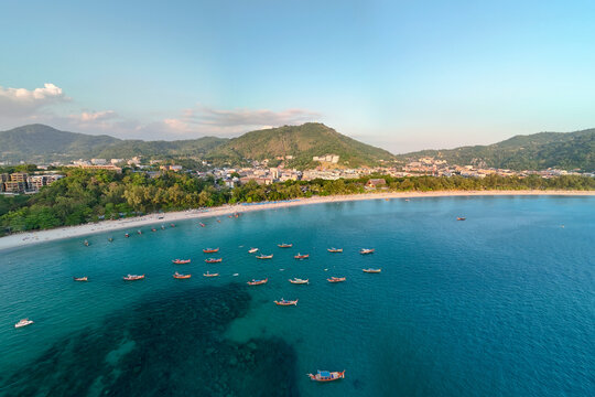 Overlooking Kata Beach in Thailand, traditional longtail boats drift peacefully on shimmering turquoise waters