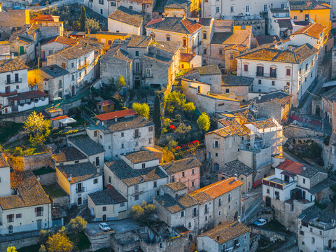 Aerial view of historic stone houses and terracotta rooftops bathed in golden sunset light in Capestrano, Abruzzo, Italy.