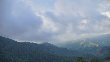 Naklejka premium Beautiful mountain landscape under a dramatic cloudy sky with sunlight hitting the green hills.