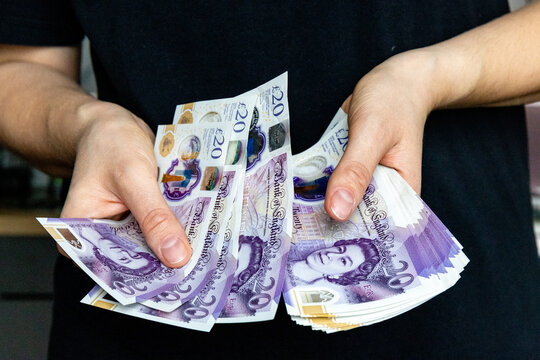 A stack of twenty pound banknotes from the Bank of England featuring Queen Elizabeth II in hands of a woman
