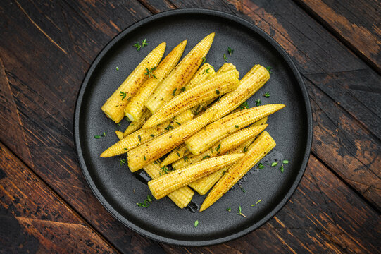 Golden fried baby corn with thyme served on black plate rustic vegetarian dish on dark wooden background