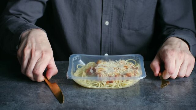 Conceptual video showing man in shirt waiting for his meal, receiving prepackaged pasta with parmesan preparing to eat it with golden cutlery on dark textured table. Unhealthy convenience food concept