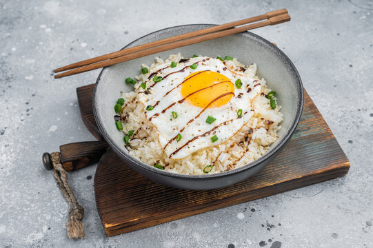 Minimal rice bowl with fried egg, herbs, and sweet glaze photographed on a modern gray surface for stylish culinary content.