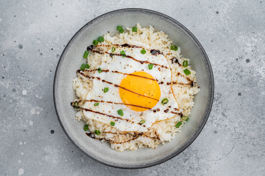 Minimal rice bowl with fried egg, herbs, and sweet glaze photographed on a modern gray surface for stylish culinary content.