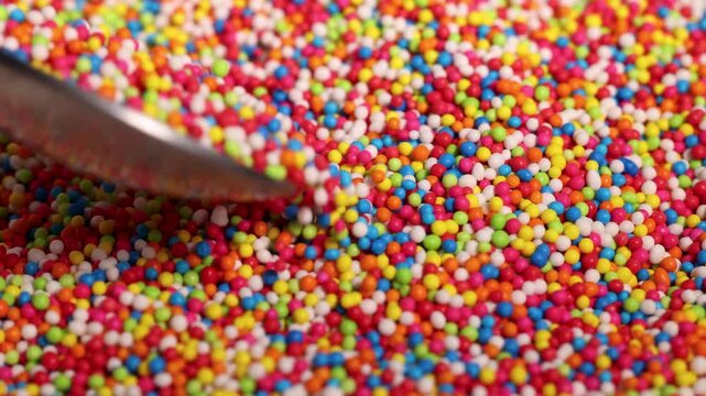 A close up view of colorful candy sprinkles being stirred by spoon in slow motion making for dynamic and sweet visual.