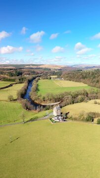 The River Esk winds through green fields and dense trees in the Scottish Borders. This scene shows a clear view of the landscape near Langholm on the A7. Hills rise in the background