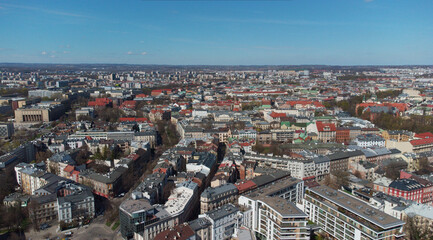 Obraz premium Wide aerial drone panorama of Krakow, Poland featuring dense urban cityscape, historic architecture, residential buildings, rooftops, and skyline under blue sky. Elevated polish city.