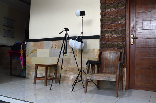 A quarter-right perspective showing a professional softbox on a tripod stand placed on a tiled porch next to traditional wooden furniture for an outdoor photo shoot.
