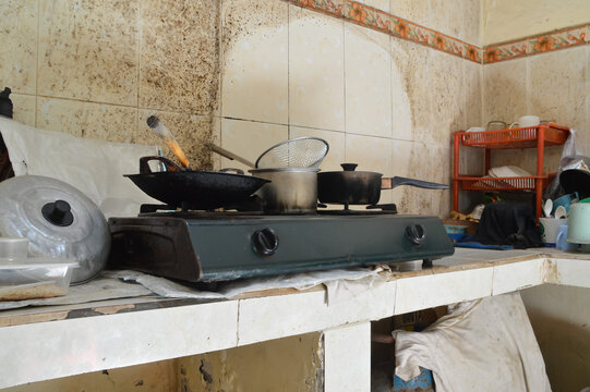 A quarter-left angle shot featuring a stainless steel water heating pot and a frying pan placed on a double burner gas stove in a domestic kitchen setting.