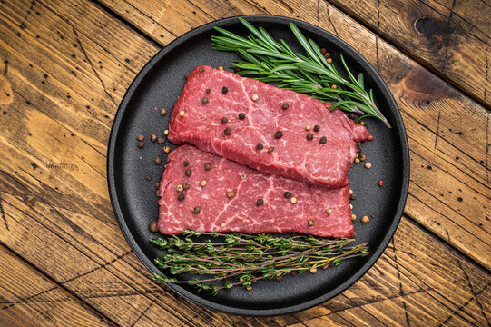 Fresh uncooked wagyu beef top round with rich marbling cooked style setup. Cast iron pan on rustic wood background.