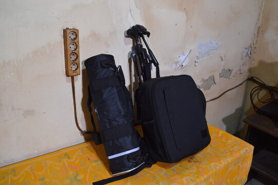 A quarter-left high angle perspective of professional camera bags and a long tripod carrier resting on a vibrant yellow tablecloth against a simple indoor wall.