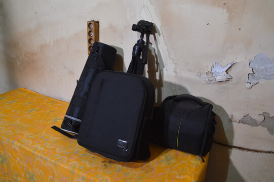 A quarter-right elevated view looking down at a collection of black camera backpacks and a tripod bag arranged neatly on a yellow cloth-covered surface.