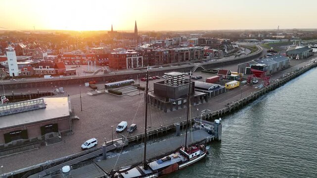 Gentle aerial turn framing Barthuis, a flat boat, lighthouse and sunlit church towers.