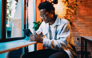 Obraz premium Smiling man using stylus and tablet by window, capturing the essence of creative tech freedom, mobile design work and digital lifestyle in an urban mobile‑first workspace.