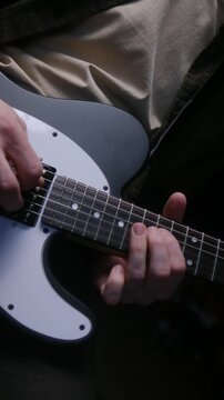 Detailed close up shot of a guitarist's hands passionately playing a riff on a white and gray electric guitar, focusing on the intricate fingerwork on the fretboard and strumming technique. Vertical
