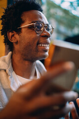 Close-up of a cheerful man laughing during a phone call outside a cafe, highlighting authentic...