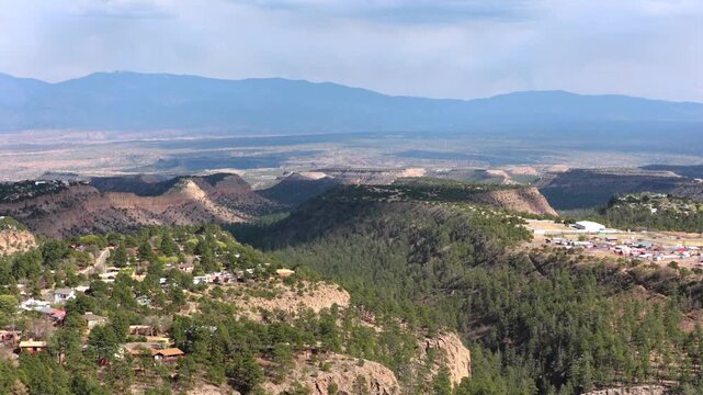 Drone view captures the rugged beauty of Los Alamos, New Mexico. Deep canyons carved through volcanic mesas are covered in dense ponderosa pine forests, perfect for adventure travel.