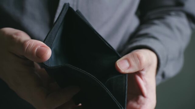 Destitute man hands opening black wallet with no money inside, representing personal financial crisis, unemployment, debt, poverty, bankruptcy in close up. Broke man opening, showing his empty wallet