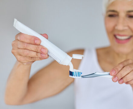 Portrait of an elderly senior woman is cleaning brushing his teeth in front of mirror in bathroom. Dental hygiene, vitality and beauty concepts