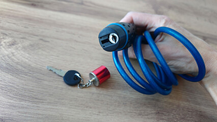 Naklejka premium Holding a blue coil lock with key in hand on wooden surface
