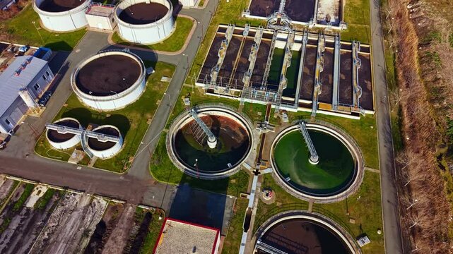 The scene shows a water treatment facility with multiple circular tanks and large structures. It is bright and clear outside, showing the layout of the facility.