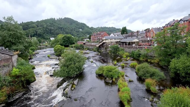 Panoramic view of river dee flowing through llangollen town in wales with historic buildings and lush green hills.