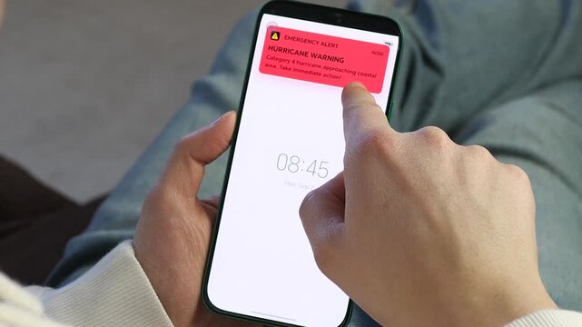 Emergency alert on smartphone. Hurricane warning notification pops up on mobile screen. Category 4 storm approaching. Essential for climate change, disaster safety, news, and emergency preparedness